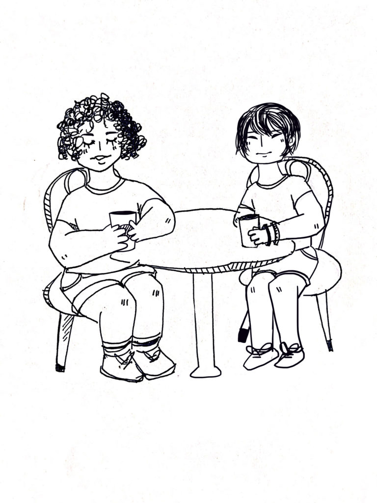 Two people with cups of coffee in their hands sit at a table and talk.
