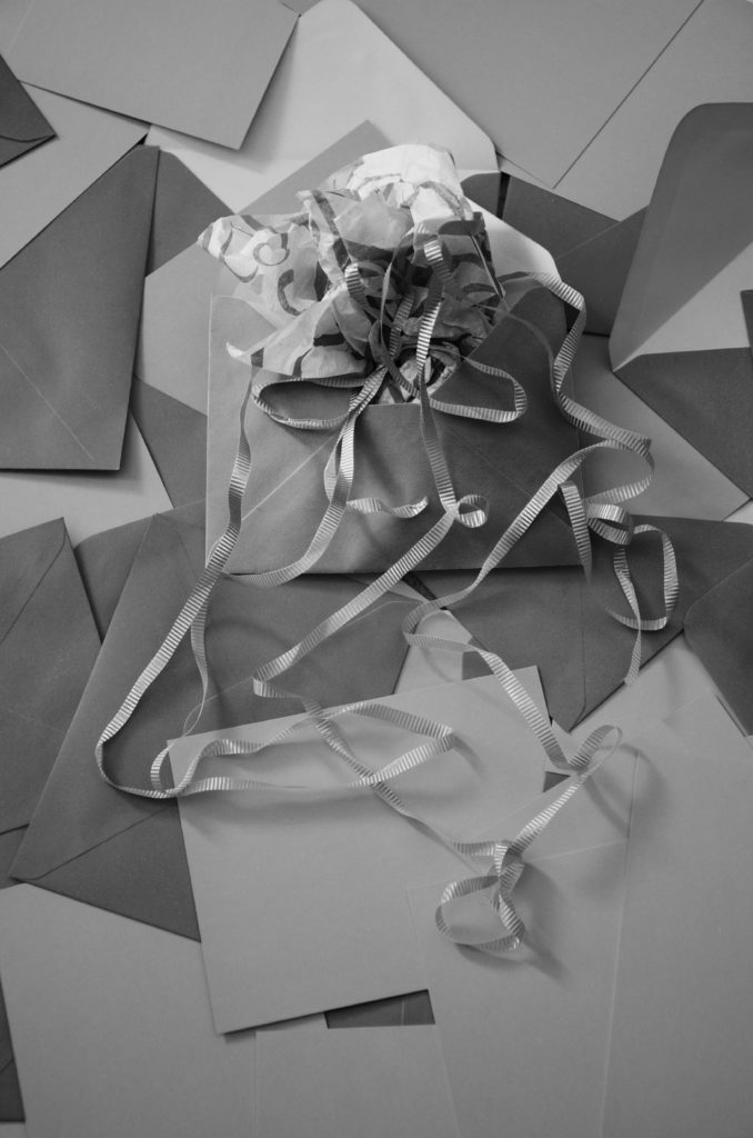 Various envelopes are scattered about on a surface. The topmost one is open and contains decorative paper and ribbons.