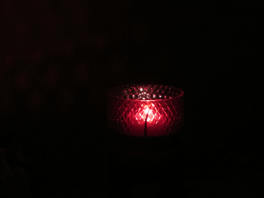 A cup of tea is shrouded in darkness, though it is lit red by a light within.