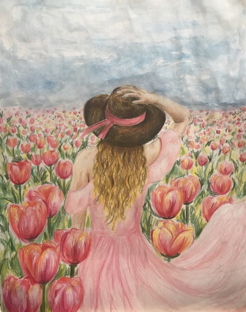 A person wearing a pink dress holds a straw hat with a pink ribbon on their head while walking through a field of tulips.